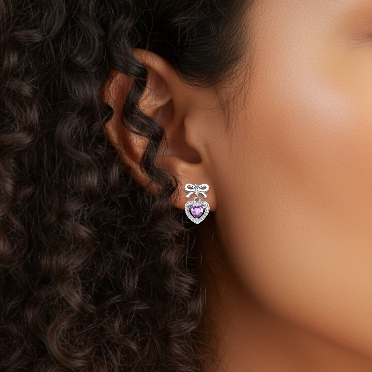 Close-up of an ear wearing a heart-shaped earring with a purple gemstone.