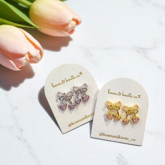 Pair of bow-shaped earrings on branded display cards with tulips in the background.