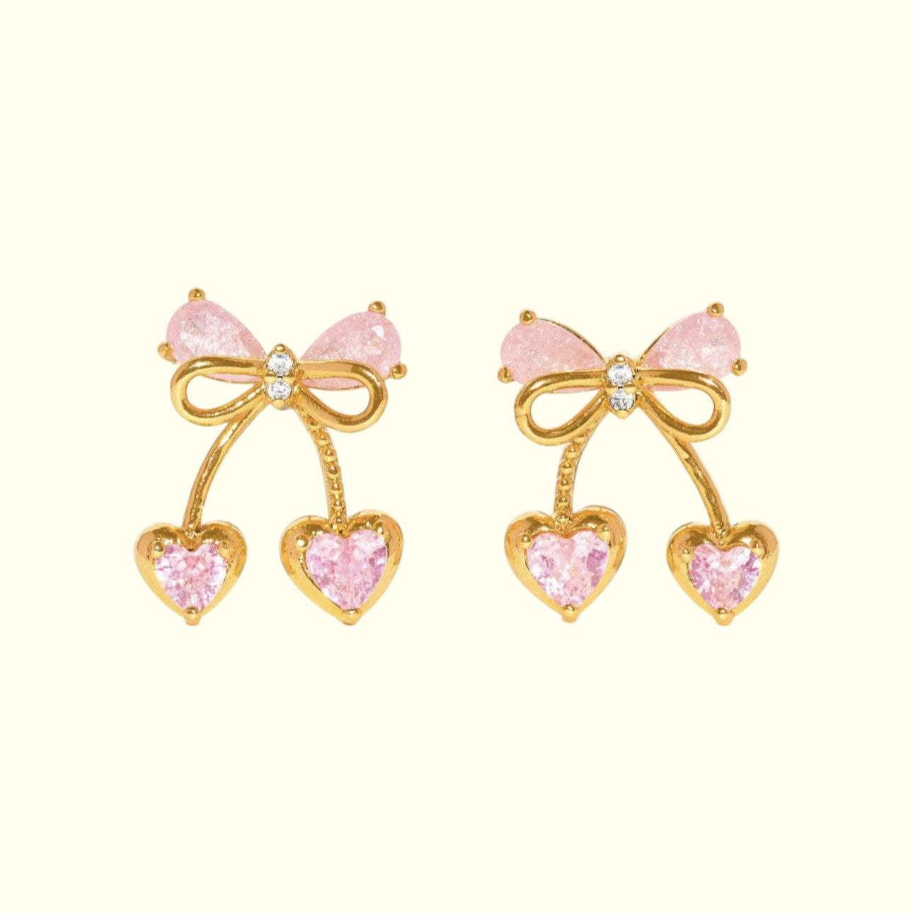 Pair of earrings with gold bows and pink heart-shaped stones on a white background