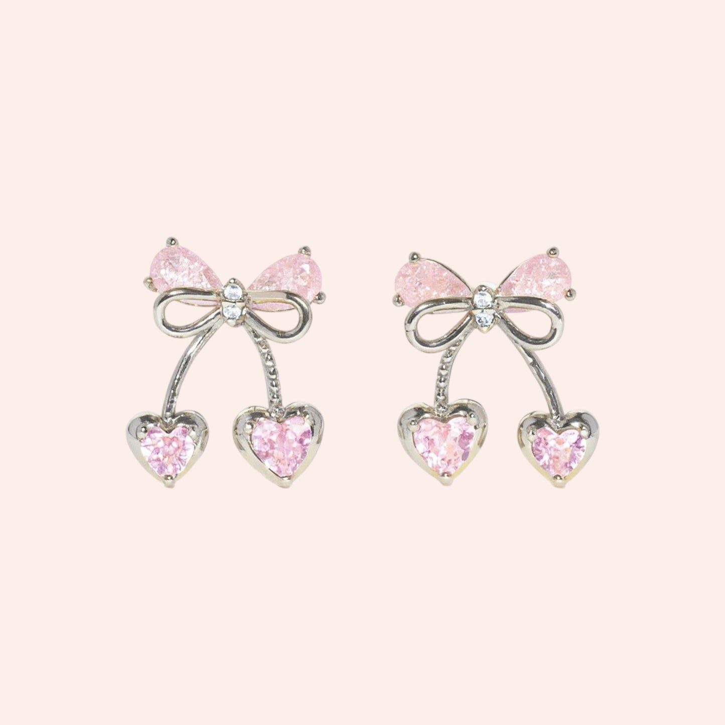 Pair of earrings with pink gemstones and bow designs on a light pink background
