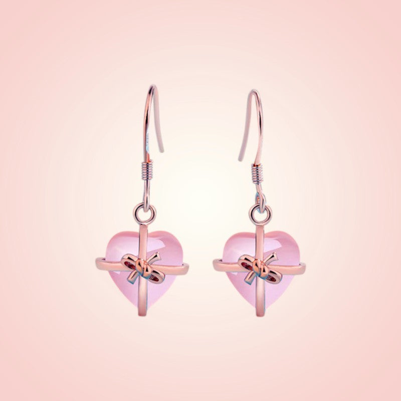 Heart-shaped earrings with pink hearts and gold bows on a pink background