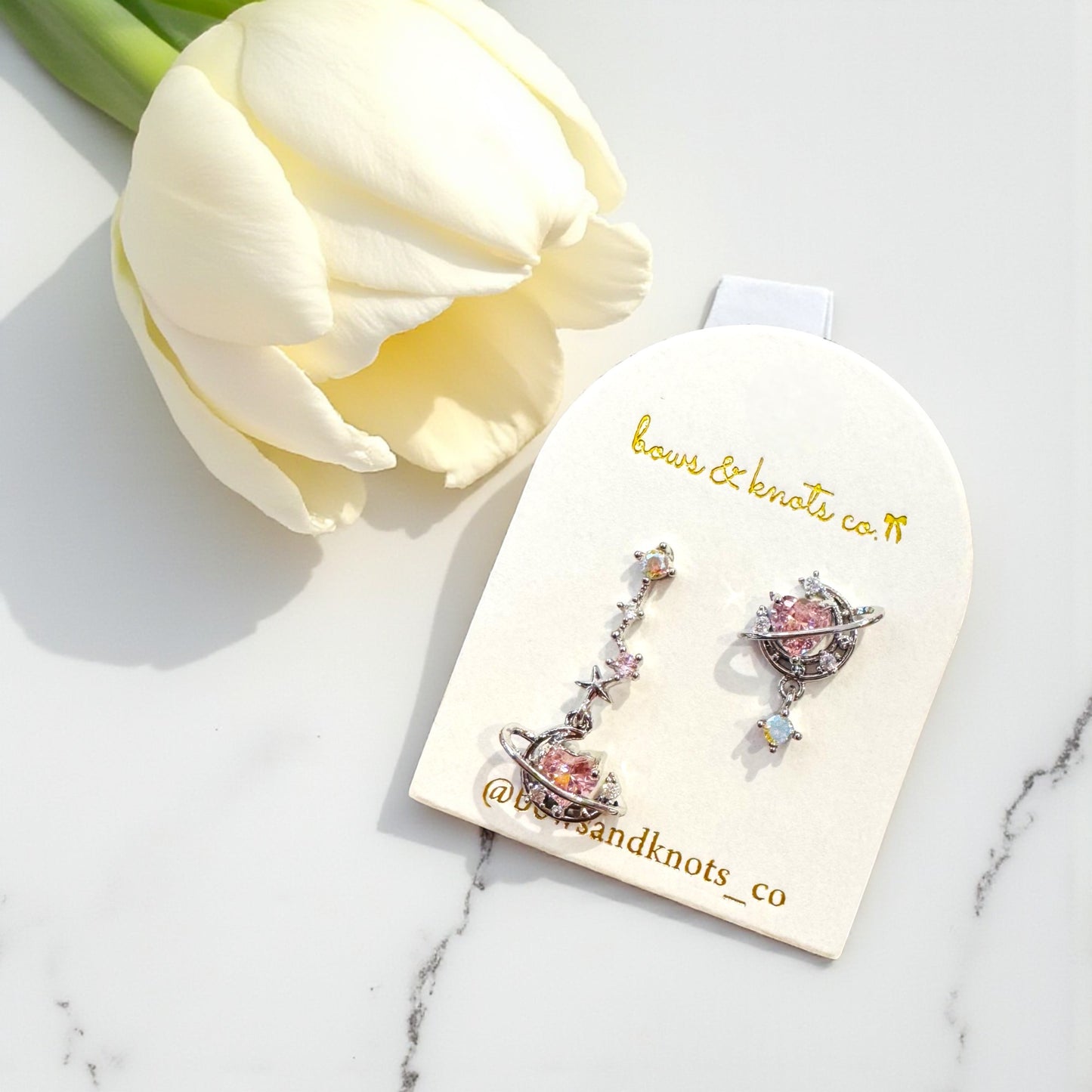 Pair of earrings on a branded card with a white tulip in the background