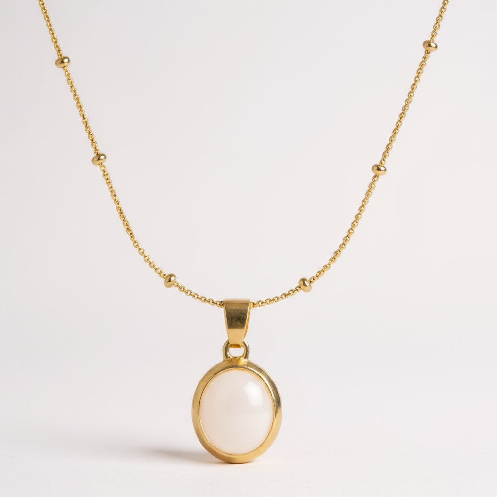 Gold necklace with a white pendant on a light gray background