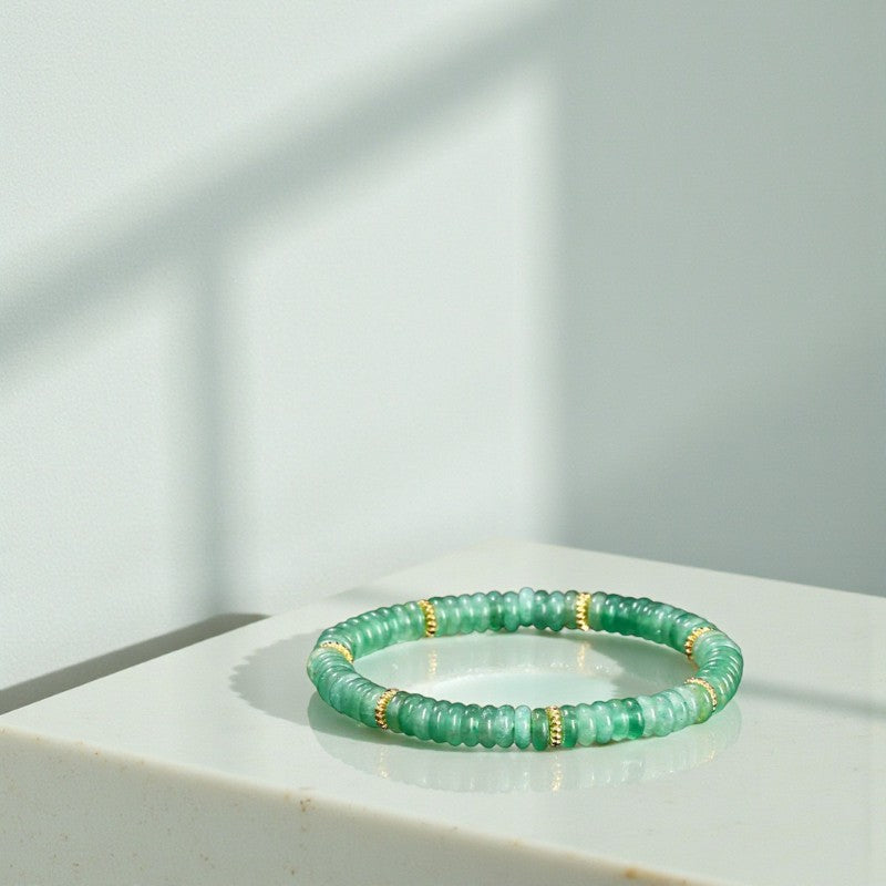 Green beaded bracelet with gold accents on a white surface