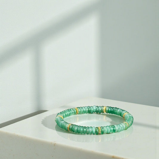 Green beaded bracelet with gold accents on a white surface