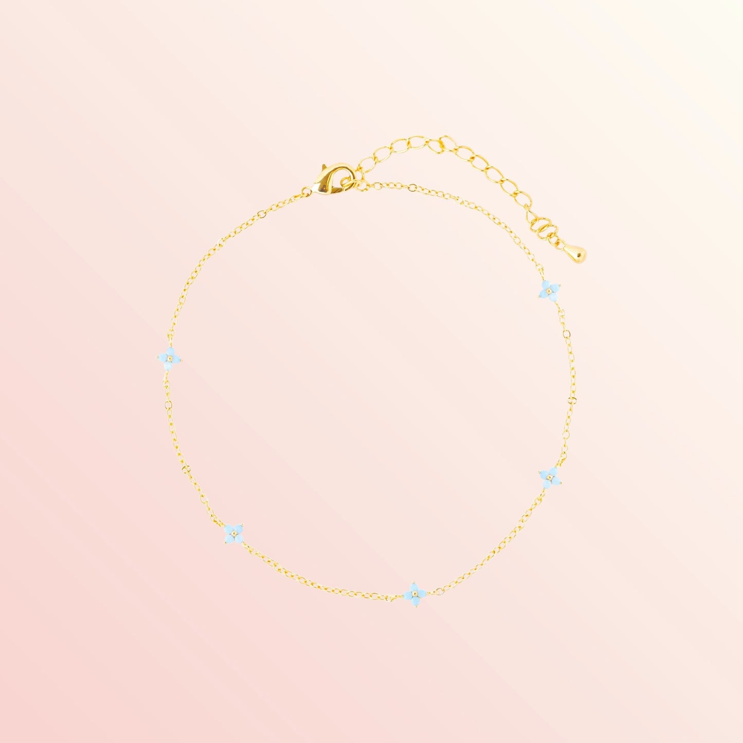 Gold bracelet with small blue stones on a light pink background