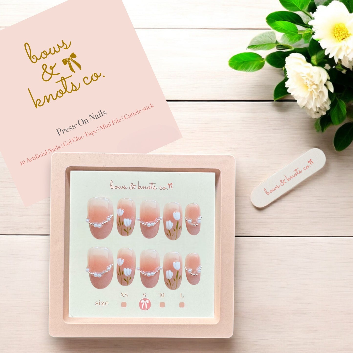 Press-on nails set with a pink box and floral design on a wooden surface.