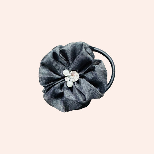 Dark gray fabric hair tie with a decorative element on a light pink background
