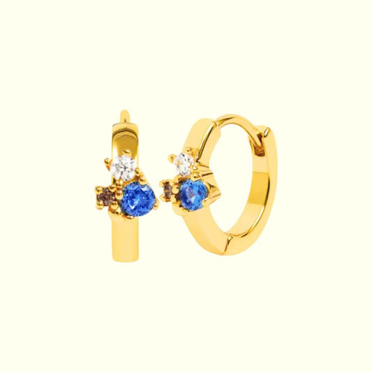 Gold hoop earrings with blue gemstones on a white background