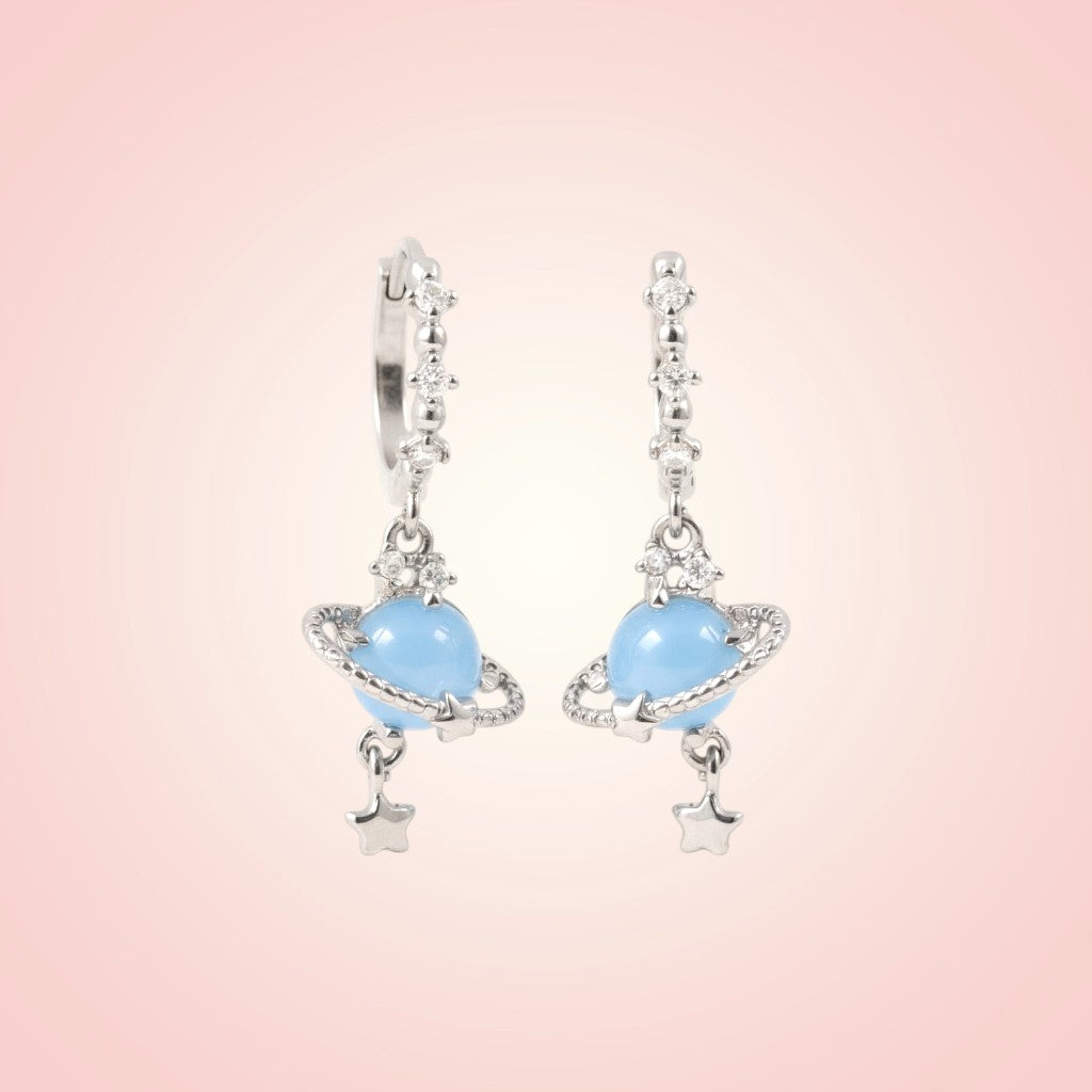 Pair of earrings with blue gemstones and star accents on a pink background