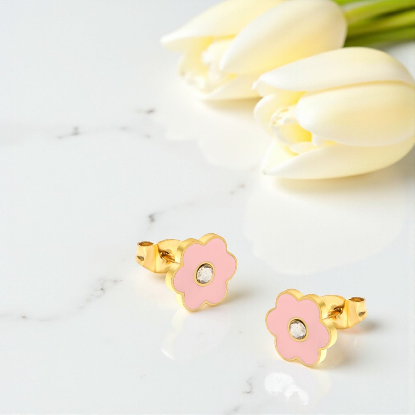 Pink flower-shaped earrings with gold accents on a white marble surface with white tulips.