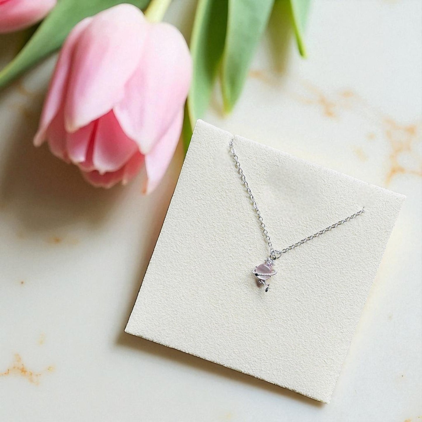 Silver necklace on a jewelry display card with pink tulips in the background