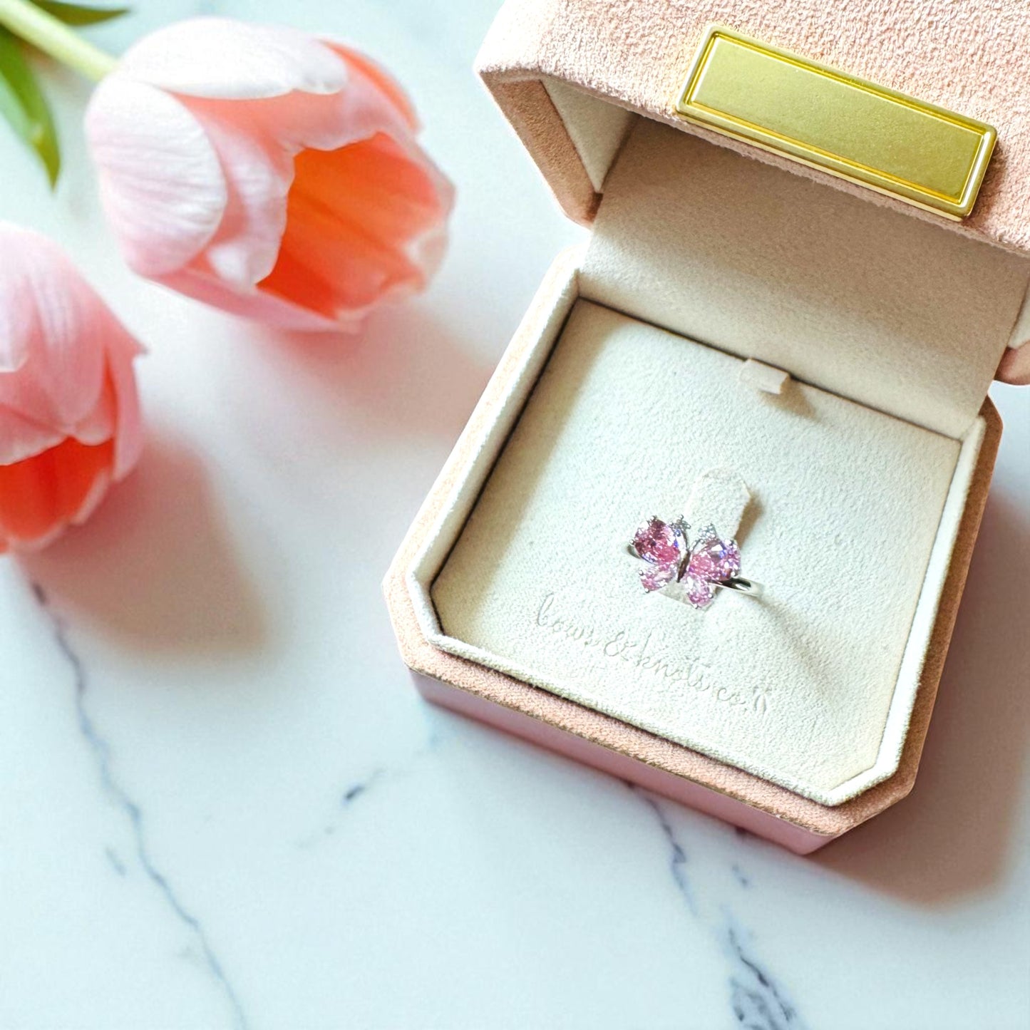 Pink gemstone ring in a jewelry box with pink tulips in the background