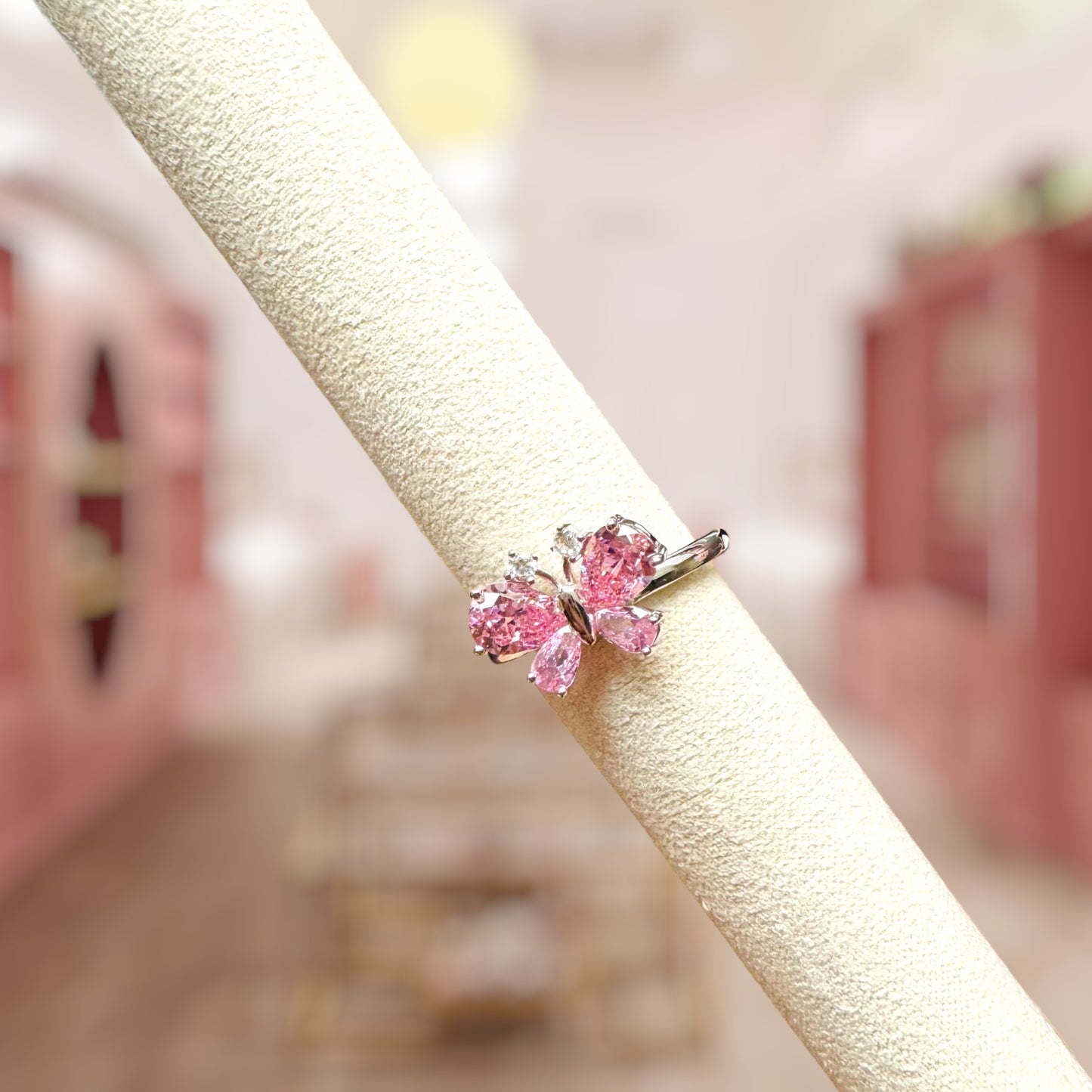 Pink butterfly-shaped earring on a beige stand with a blurred background