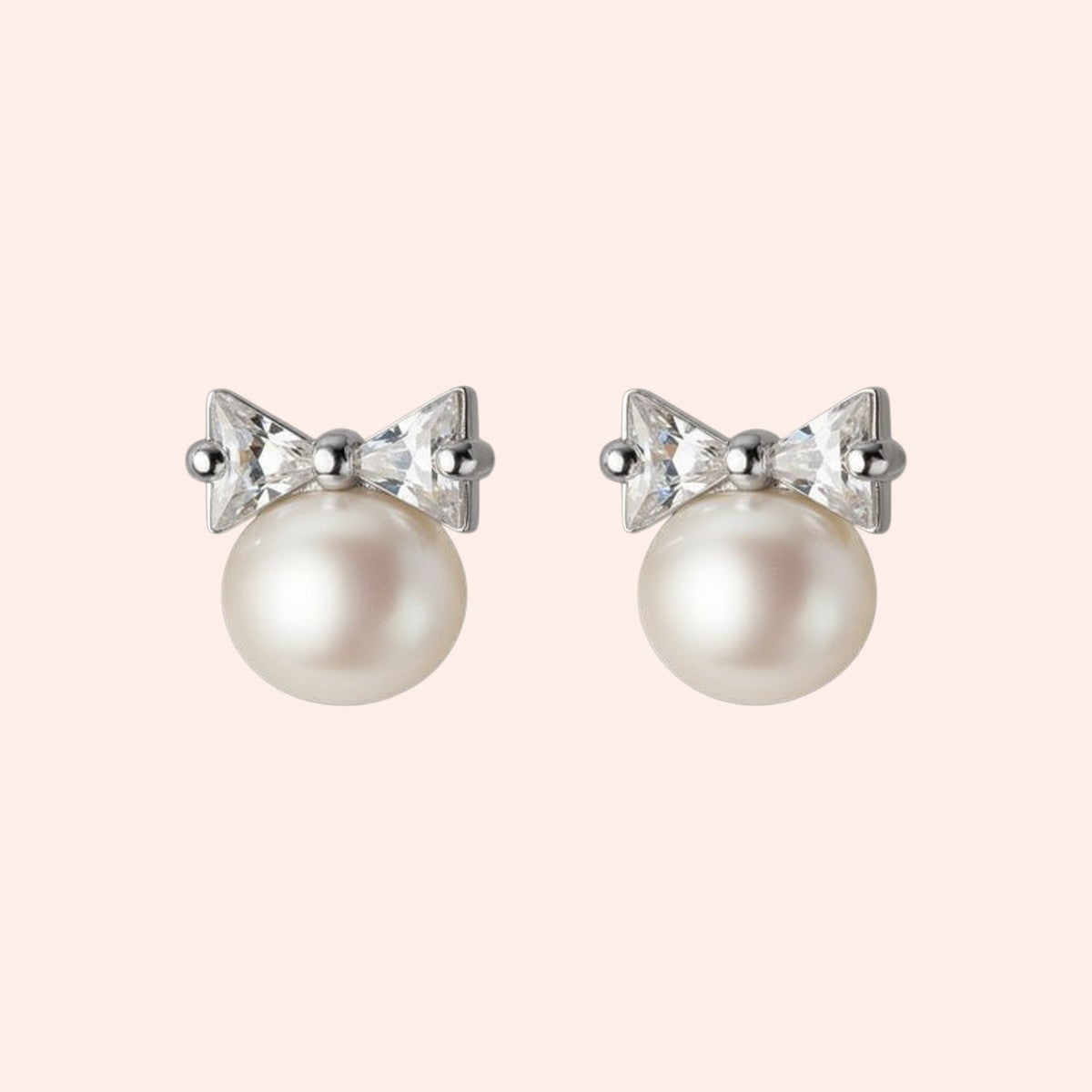 Pearl earrings with bow and crystal details on a light pink background