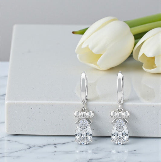 Silver teardrop earrings with bow accents on a marble surface with white tulips.