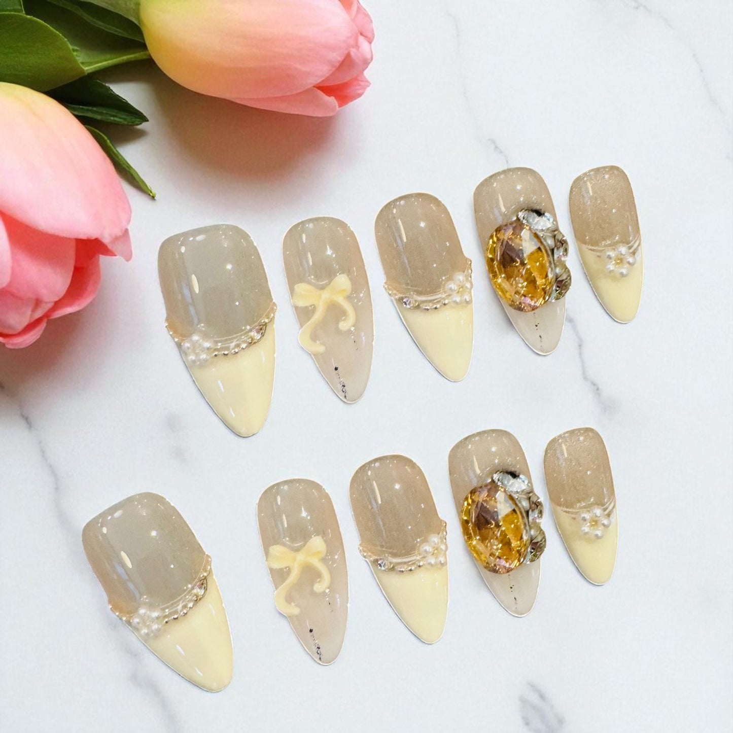 Decorative nail art with gemstones and bows on a white surface with pink tulips.