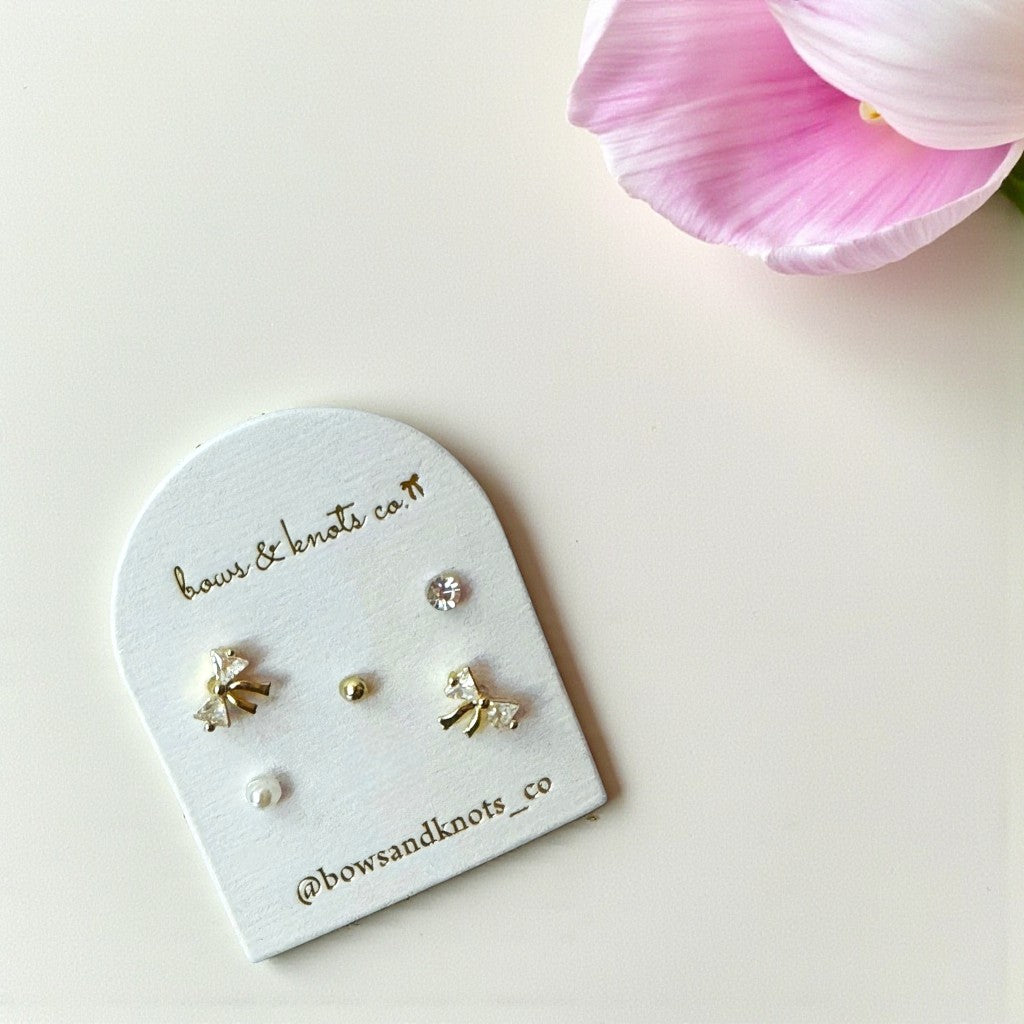 Set of earrings on a branded display card with a pink flower in the background
