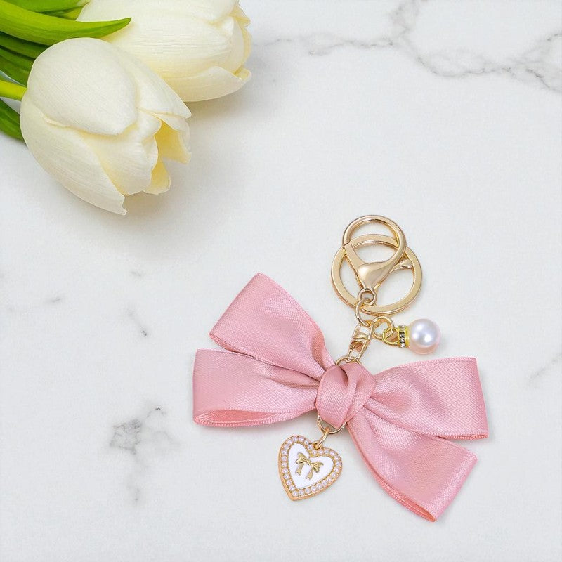 Pink bow keychain with heart charm on a marble surface with white tulips.