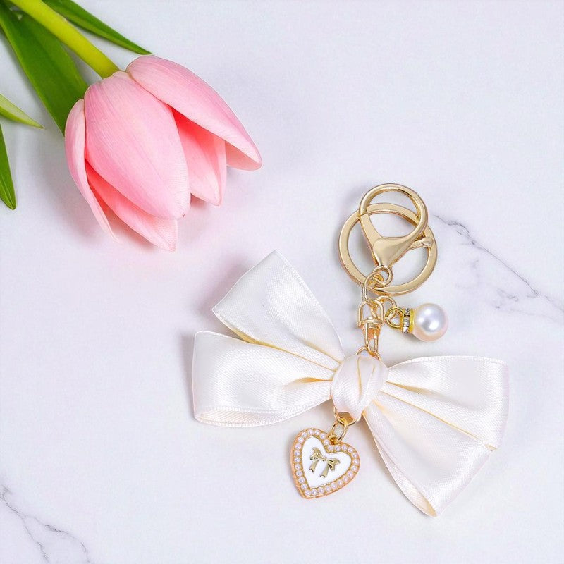 Keychain with bow and heart charm next to a pink tulip on a marble surface