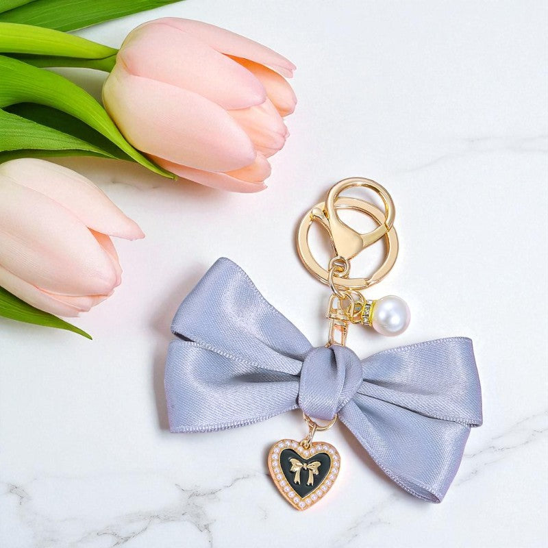 Keychain with a bow and heart charm on a marble surface with pink tulips.