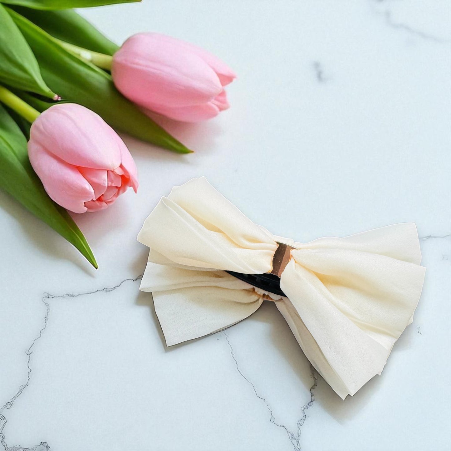 Cream-colored bow tie on a marble surface with pink tulips