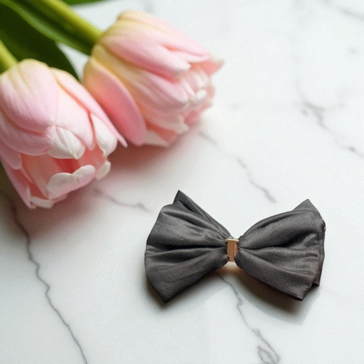 Gray bow tie on a marble surface with pink tulips in the background