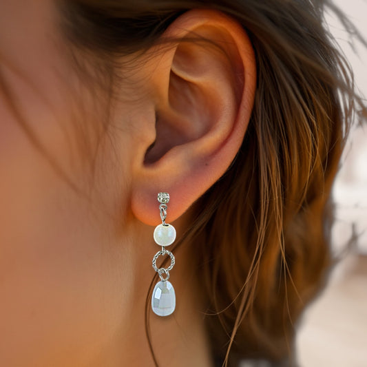 Close-up of an ear wearing a silver earring with a white gemstone.