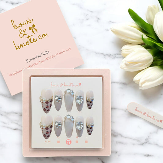 Set of press-on nails in a box with 'bows & knots co.' branding on a marble surface with tulips.