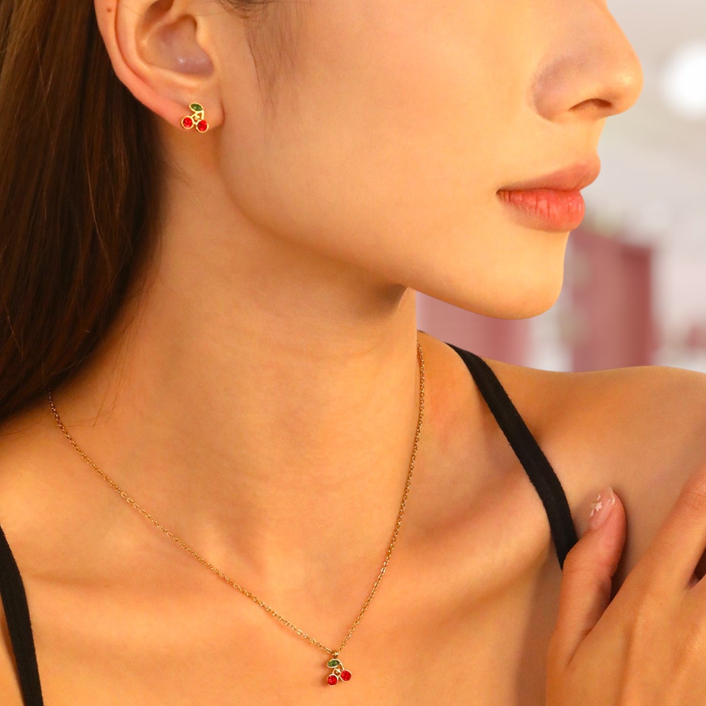 Close-up of a woman wearing a gold necklace with a cherry pendant.