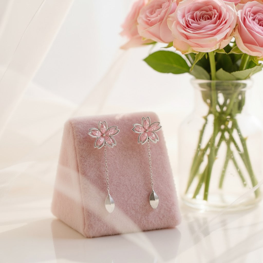 Flower-shaped earrings on a pink stand with a vase of pink roses in the background