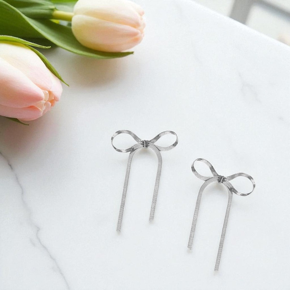 Bow-shaped earrings on a white surface with pink tulips