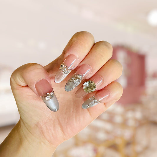 Hand with decorative nails featuring crystals and a blurred background