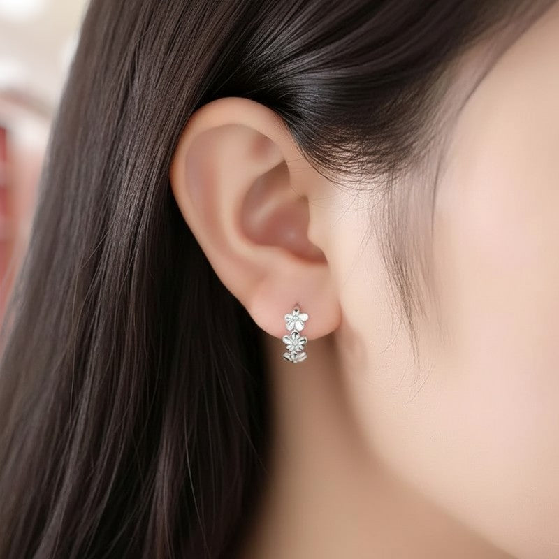 Close-up of an ear wearing a floral earring with dark hair and blurred background