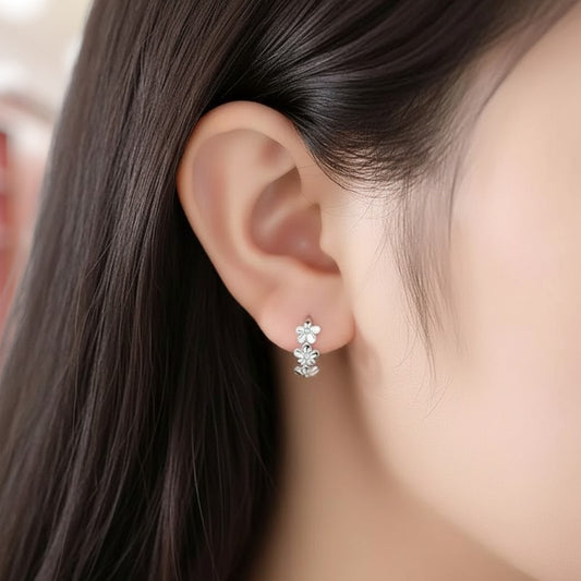 Close-up of an ear wearing a floral earring with dark hair and blurred background