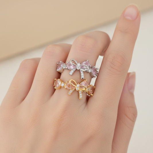 Three bow-shaped rings in gold, silver, and rose gold on a hand against a neutral background
