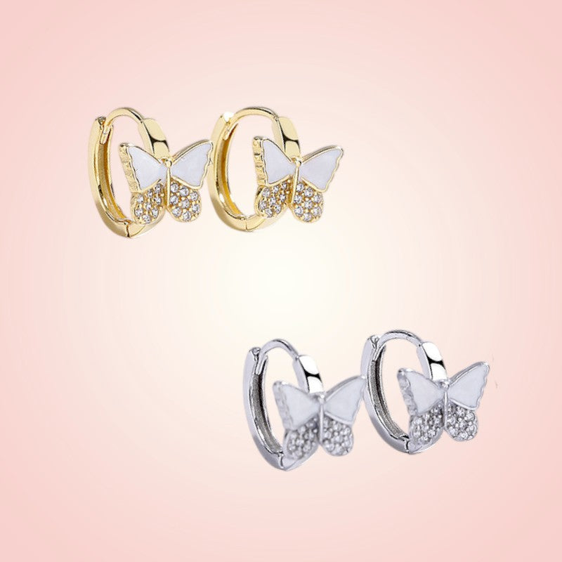 Butterfly-shaped hoop earrings in gold and silver on a pink background