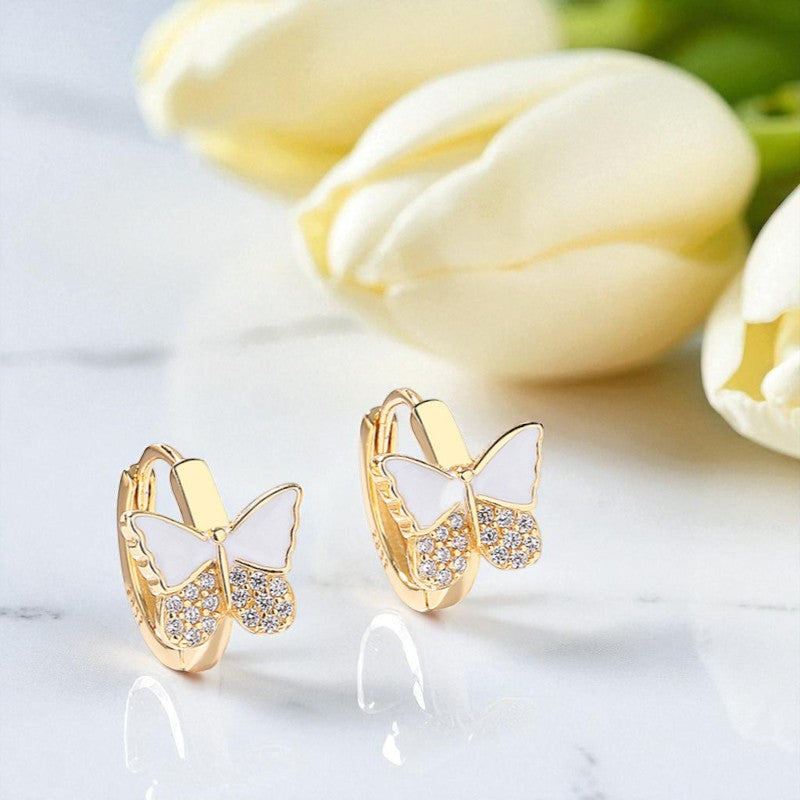 Gold butterfly earrings with diamond accents on a marble surface with white tulips in the background.