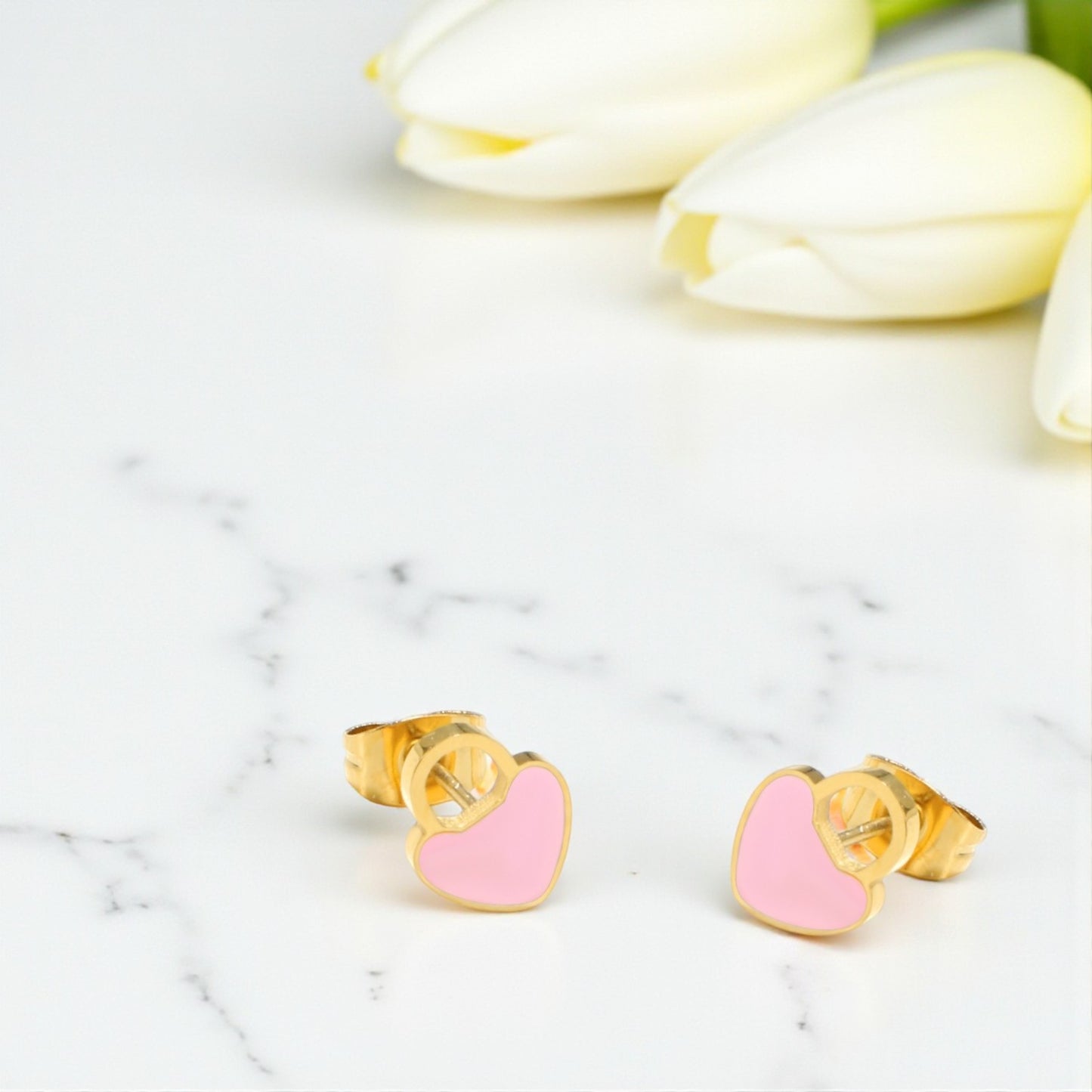 Pink heart-shaped earrings with gold posts on a marble surface.