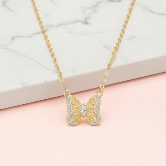 Gold butterfly necklace with gemstones on a light pink surface