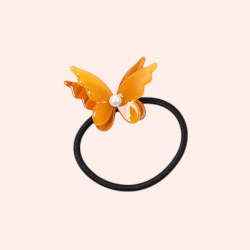 Butterfly-shaped hair tie with a pearl on a light pink background