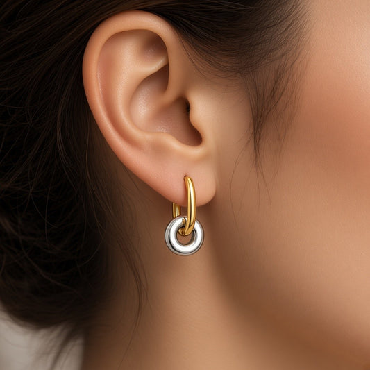A close-up of a person's ear wearing Gold and silver two-tone stainless steel hoop earrings with sculptural circular charms.