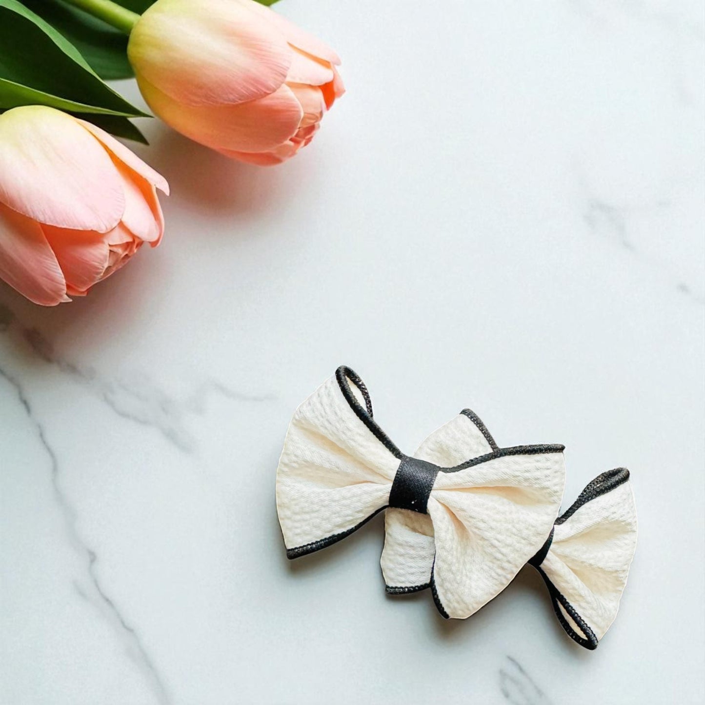 White bow with black edges on a marble surface with pink tulips.