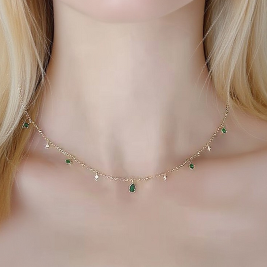 Gold necklace with green gemstones worn by a person with blurred background
