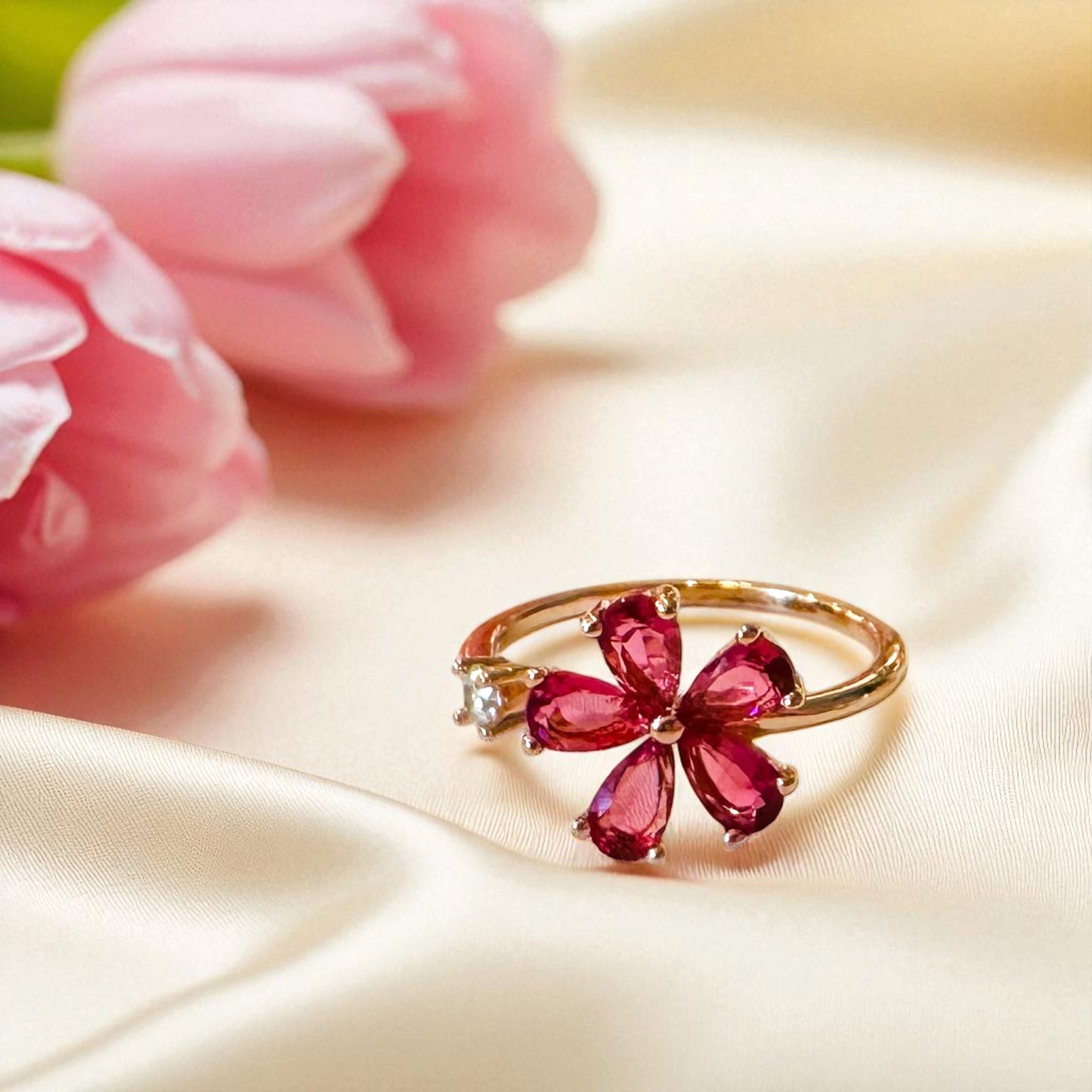 Gold ring with red gemstones on a beige fabric background with pink flowers.