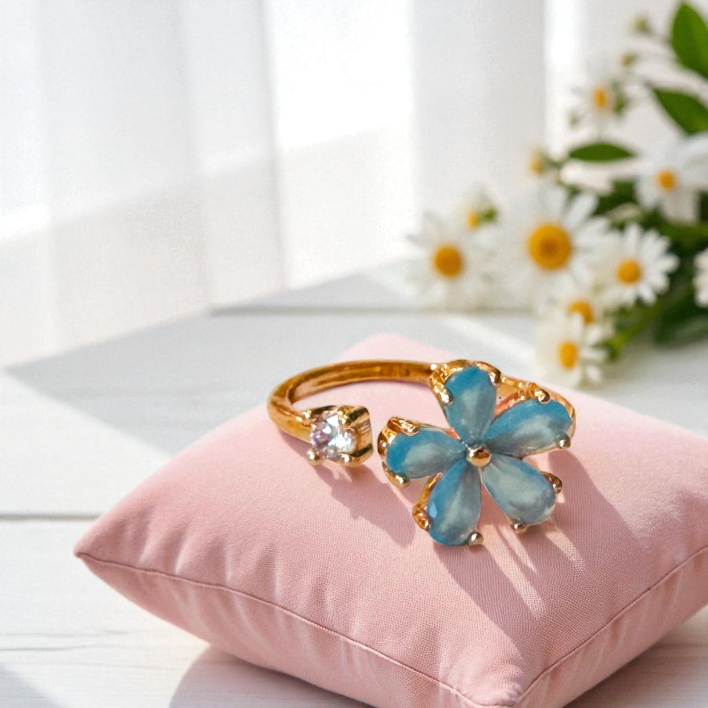 Blue flower-shaped bracelet with gold accents on a pink cushion with flowers in the background