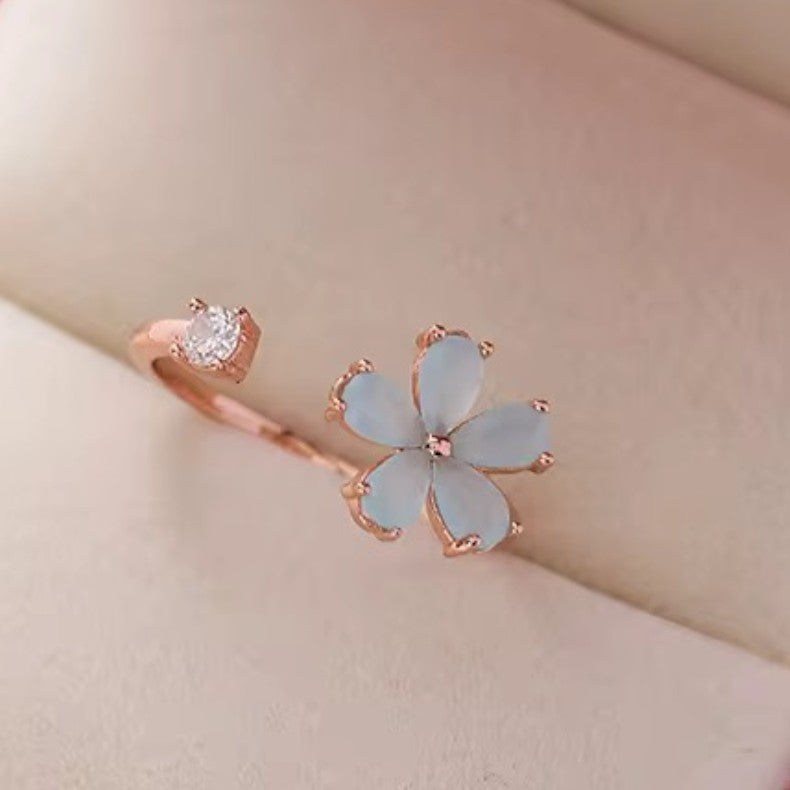Rose gold ring with a light blue flower design on a beige background