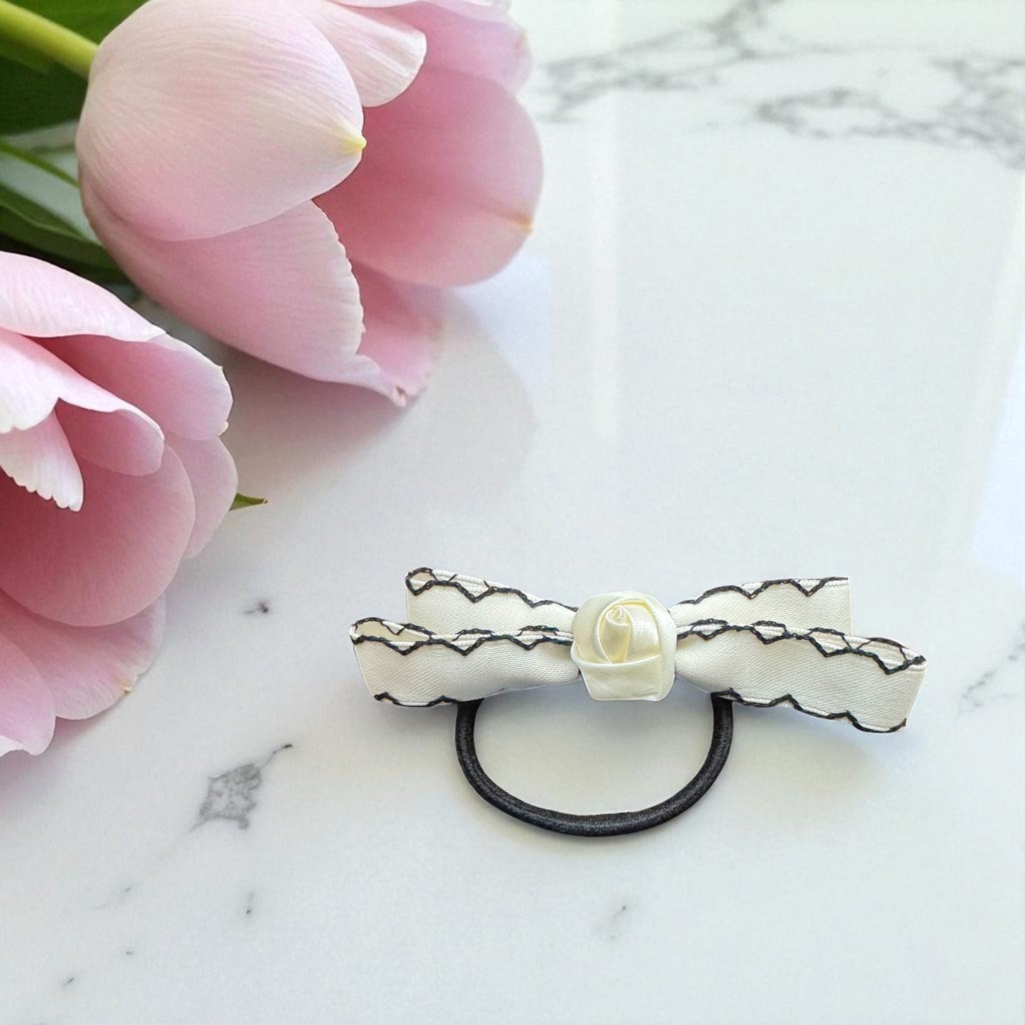 Hair tie with floral design on a marble surface with pink tulips