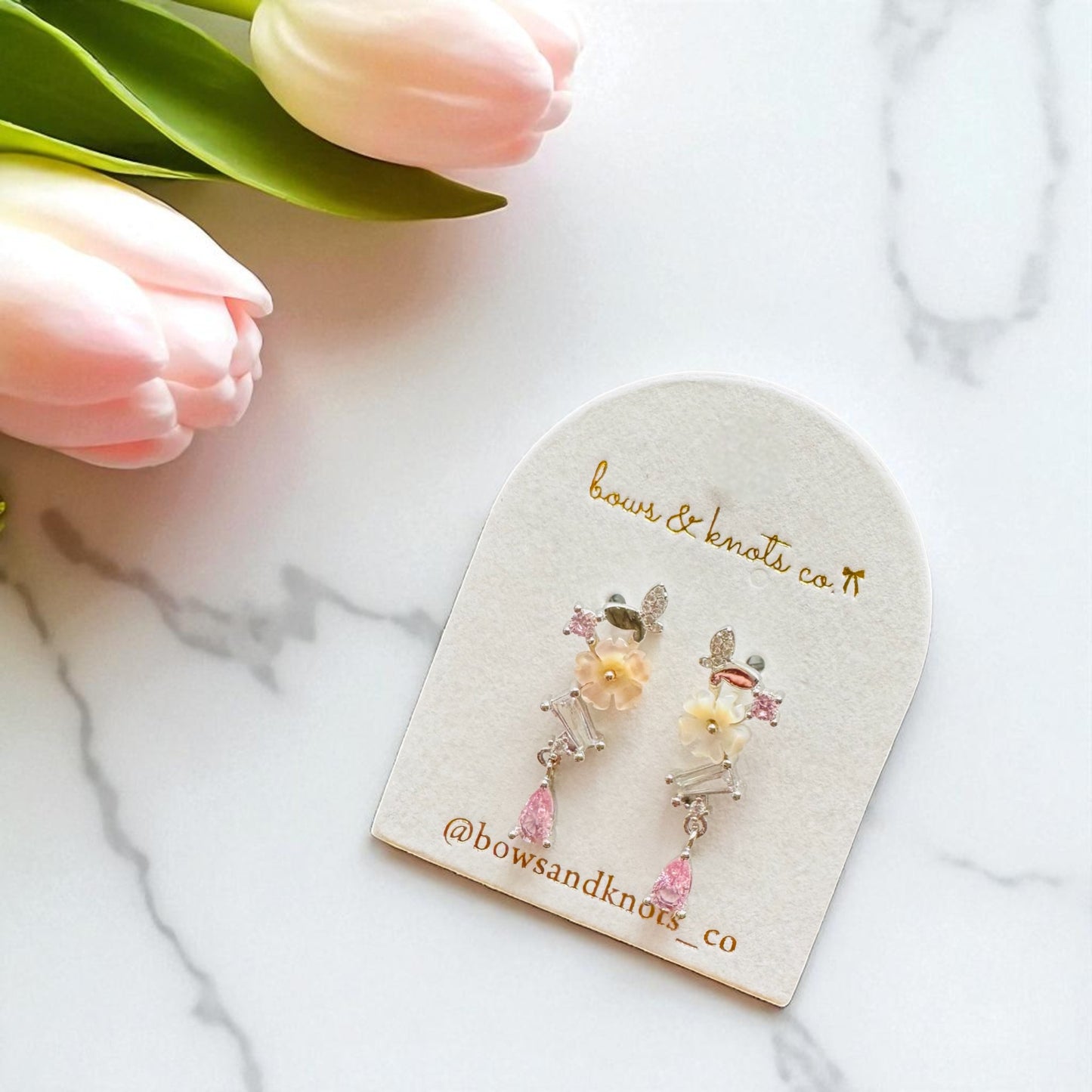 Pair of floral earrings on a branded card with tulips in the background