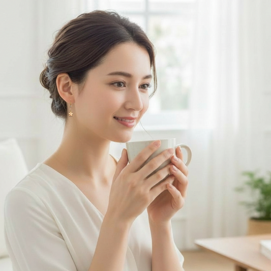 Woman holding a white mug in a bright, softly blurred indoor setting, wearing Bows and Knots Co. earrings